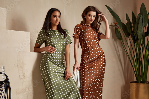 Two fashion model brunette hair wear green brown dots silk dress shoes accessory clothes date party walk interior journey summer collection plant flowerpot stairs beautiful woman tan skin friends.