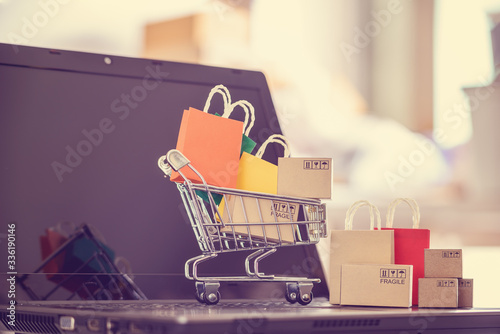Online shopping / e-commerce and customer experience concept : Shopping cart with boxes, shopping bags on a computer, depicts consumers / buyers buy or purchase goods and service from home photo