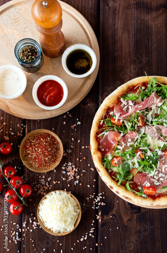 Italian pizza with arugula, cheese, ham. Top view. Pizza sauce, cherry tomatoes, salt, basil