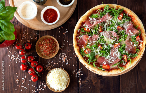 Italian pizza with arugula, cheese, ham. Top view. Pizza sauce, cherry tomatoes, salt, basil