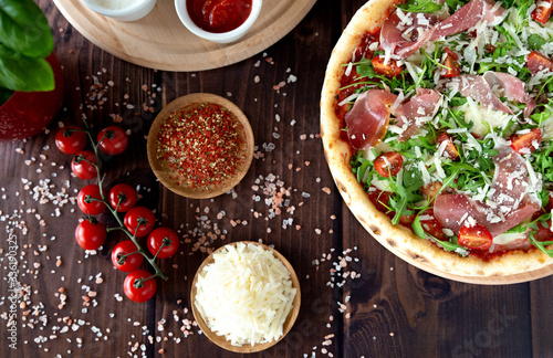 Italian pizza with arugula, cheese, ham. Top view. Pizza sauce, cherry tomatoes, salt, basil
