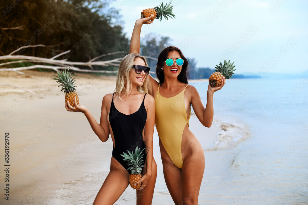 two incredibly beautiful sexy girl models in a bikini on the sea shore of a tropical island pineapple, blonde brunette, bronze tan, travel summer vacation, fashion style - obrazy, fototapety, plakaty 