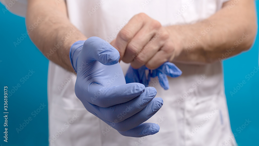 A male doctor surgeon in white uniform puts on blue gloves. A male doctor surgeon in white uniform puts on blue gloves.