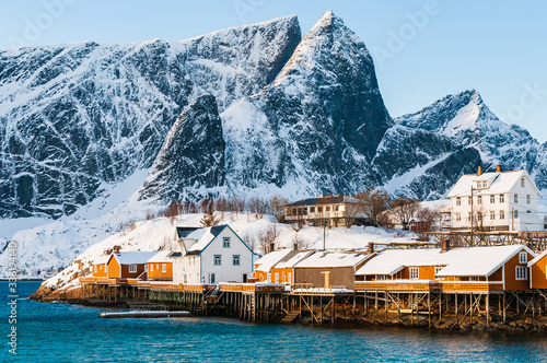 Buildings at waterfront in front of snow covered mountains. Sakrisøy, Norway.