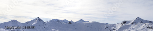 Panorama of high winter mountains with snowy slopes and sunlit cloudy sky © BSANI