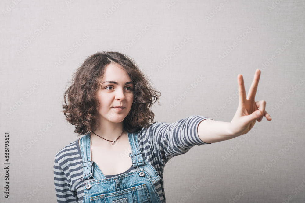 A woman makes a gesture of victory. Gray background A woman makes a gesture of victory. Gray background