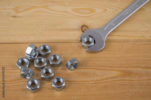 Metalowe nakrętki i klucz ułożone na drewnianej desce
