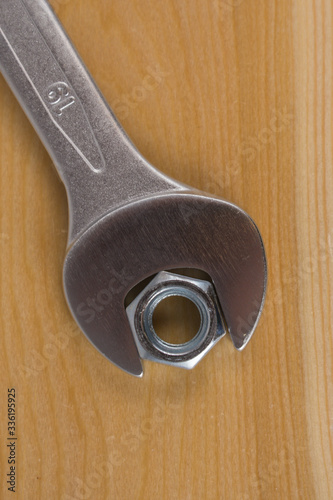 Metalowy klucz, oraz nakrętka ułożone na drewnianej desce.
