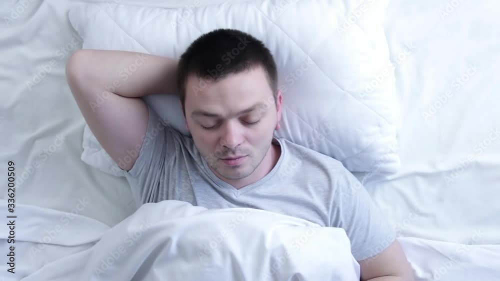 Attractive man with a beard sleeping in the bed at home. Top view of young man is sleeping in the bed. Concept of rest and sleep Attractive man with a beard sleeping in the bed at home. Top view of young man is sleeping in the bed. Concept of rest and sleep