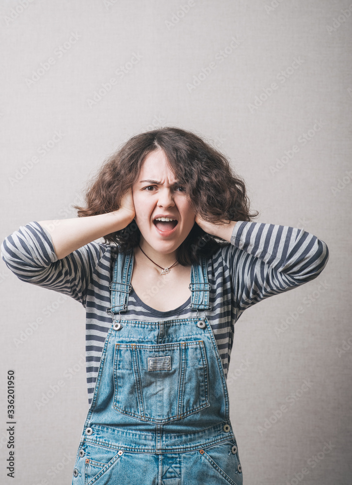 Young woman covering her ears over gray background Young woman covering her ears over gray background