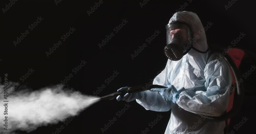 Caution Disinfection is in Progress. A man in a protective suit, glasses and a respirator sprays a disinfectant. At the same time, he makes gestures symbolizing the ban on presence