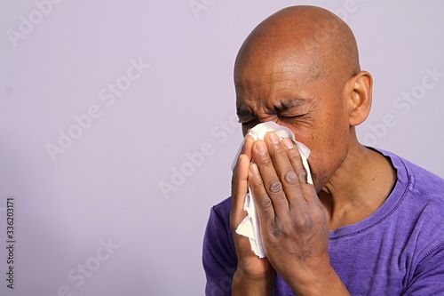 COVID-19 Coronavirus pandemic outbreak man blowing his nose fighting the disease with grey background stock photo