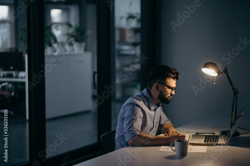 Concentrated businessman working in dark office with light from table lamp