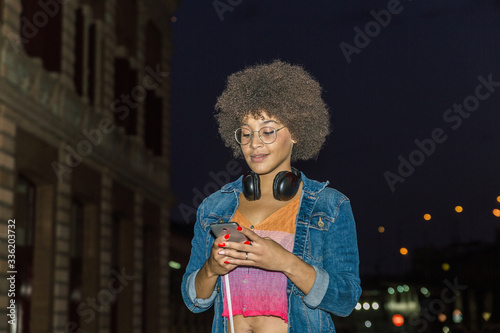 Young woman with afro curly hair and headphones around her neck looks at her mobile phone