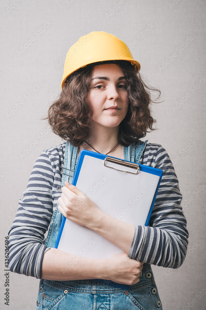 Young architect woman in yellow safety helmet holding work plan sheet, on gray background Young architect woman in yellow safety helmet holding work plan sheet, on gray background