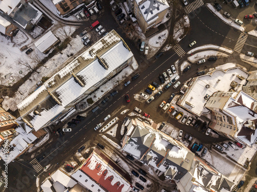 Aerial black and white winter top view of modern city with tall buildings, parked and moving cars along streets with road marking. Urban cityscape, view from above.