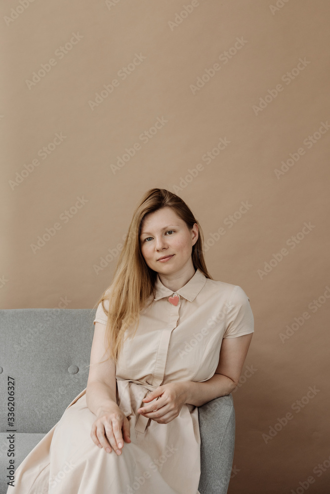 Portrait of beautiful woman wearing beige dress sitting on sofa. Portrait of beautiful woman wearing beige dress sitting on sofa.
