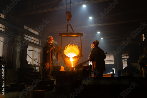 Men filling mold with melted metal in factory