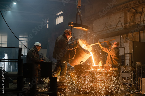 Factory workers pouring sparkling metal into mold