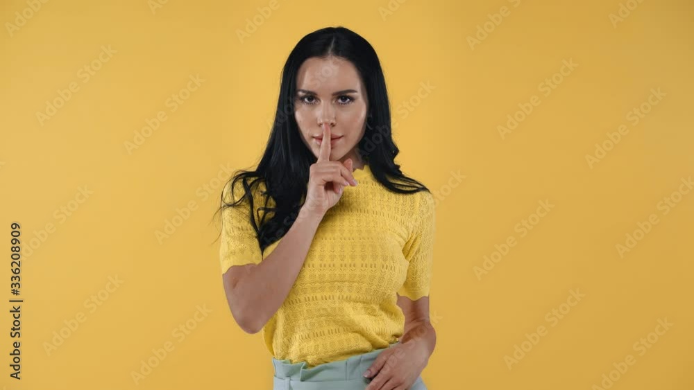 Attractive girl showing quiet gesture and smiling at camera isolated on yellow Attractive girl showing quiet gesture and smiling at camera isolated on yellow