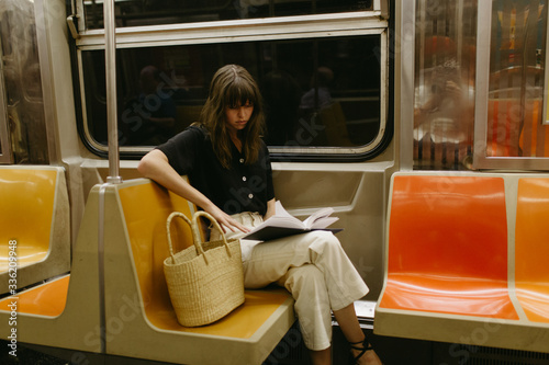 Woman with bangs sitting reading on a subway car with a basket