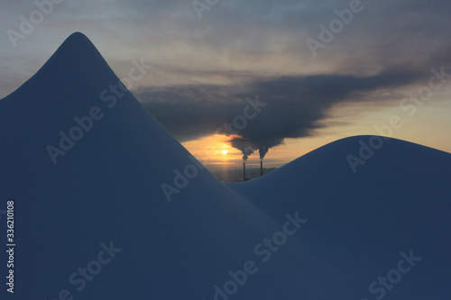 Smoking pipes against the background of the setting sun and snowdrifts