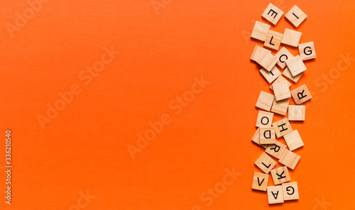 Pile of wooden letters on the surface of a orange paper background, selective focus