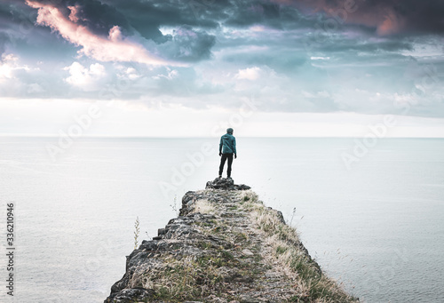 Guy in casual clothes is standing on the edge of historical structure and looks to the right with sea and dramatic sky in the background. Moody travelous blank space image. 2020