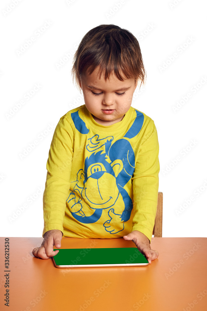 Young child girl is using tablet while sitting at table, isolated over white background Young child girl is using tablet while sitting at table, isolated over white background