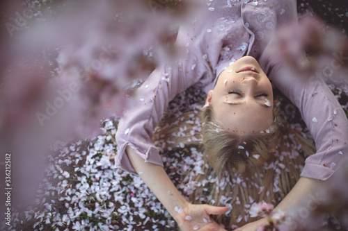 The girl enjoys the spring  the tenderness of the falling petals  a pink dress  closed eyes  blooming sakura.