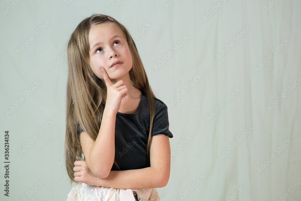 Close-up portrait of happy smiling little girl with long hair holding finger to her cheek thinking. Close-up portrait of happy smiling little girl with long hair holding finger to her cheek thinking.
