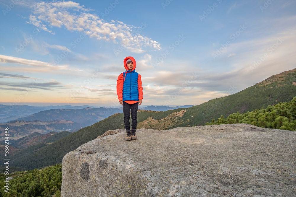 Young child boy hiker standing in mountains enjoying view of amazing mountain landscape.