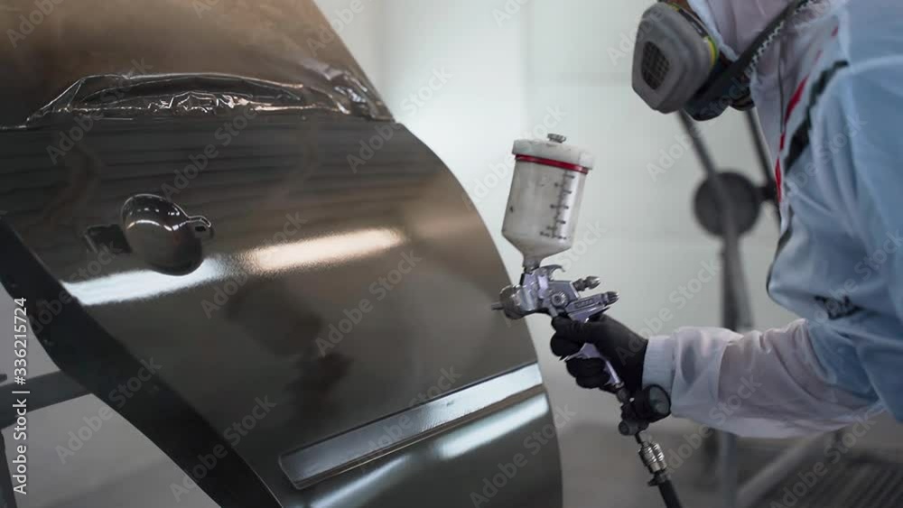 A man in a mask and a protective suit paints the car door with black paint