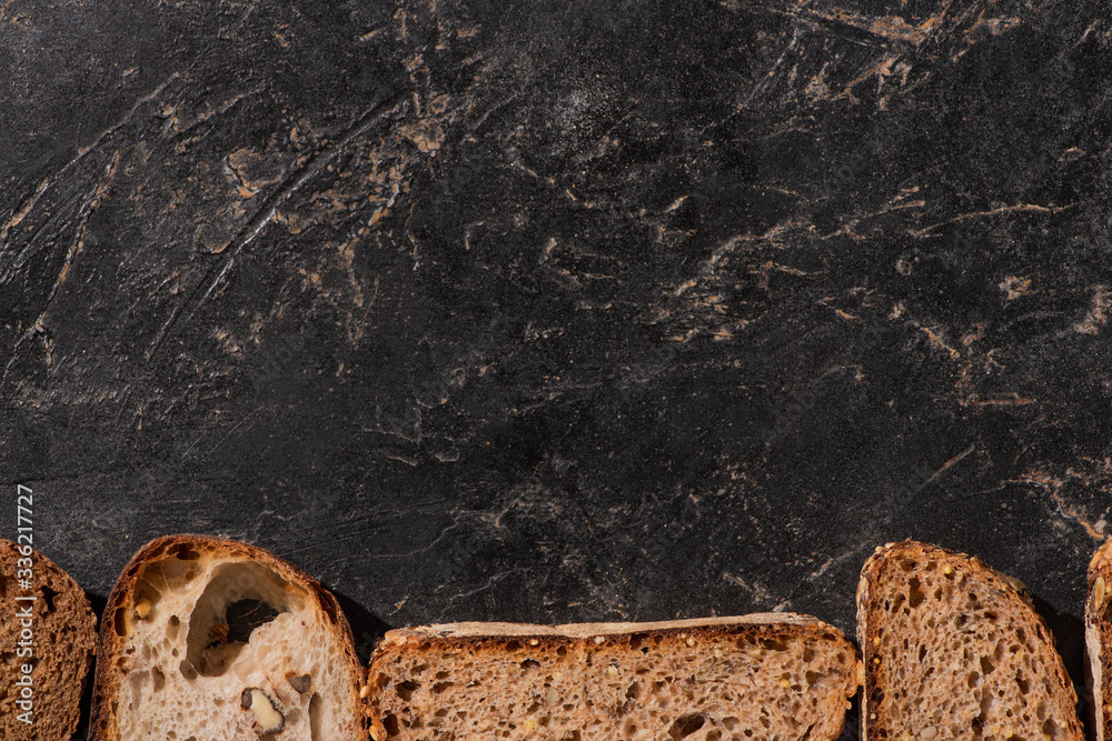 Fototapeta premium top view of fresh baked bread slices on stone black surface