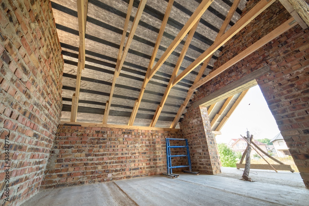 Attic of a building under construction with wooden beams of a roof structure and brick walls. Attic of a building under construction with wooden beams of a roof structure and brick walls.