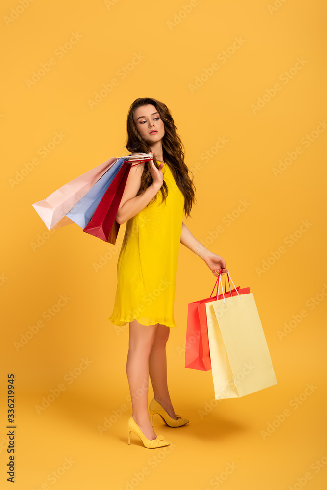 beautiful girl in spring dress holding shopping bags on yellow