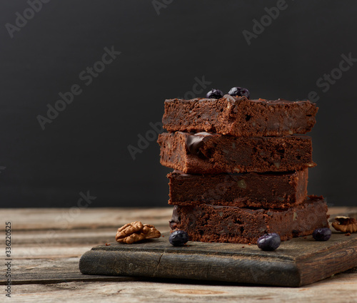 stack of square baked slices of brownie chocolate cake with walnuts on a wooden surface. Cooked homemade food. Chocolate pastry