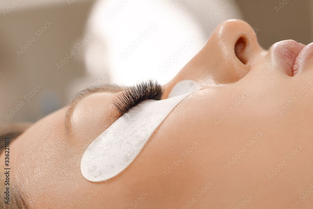 Naklejka premium Eyelashes extensions. Fake eyelashes. Eyelash extension procedure.Close up portrait of woman eye with long eyelashes. Professional stylist lengthening female lashes. Master and client in beauty salon.