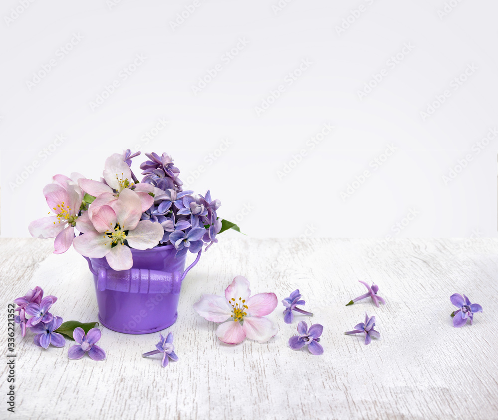 Lilac flowers and apple tree flowers in small violet bucket on a table wooden white and light background with space for text. Spring decoration Lilac flowers and apple tree flowers in small violet bucket on a table wooden white and light background with space for text. Spring decoration