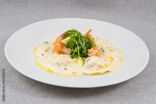 King prawns with green leaves and pasta drenched in milk sauce on a large round white plate on a gray background