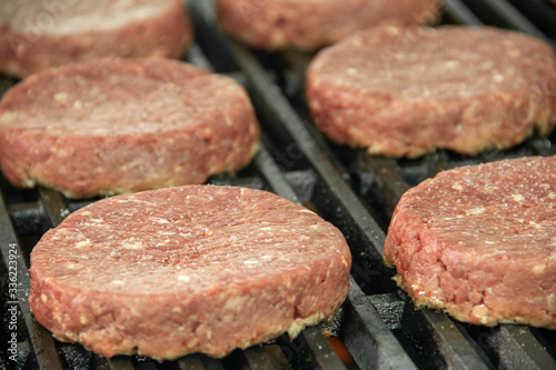 Close up of Raw hamburger patties sitting on hot char broiler grill