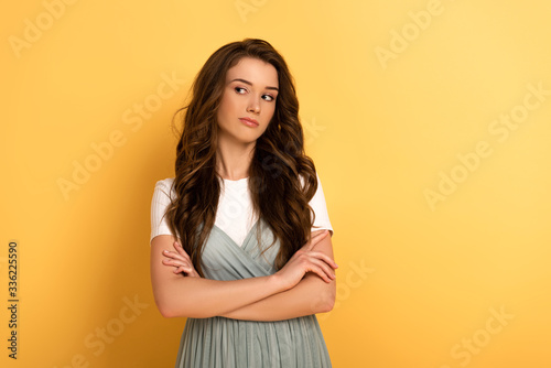 attractive thoughtful spring girl with crossed arms on yellow