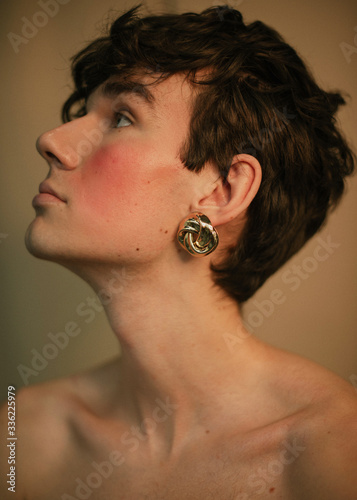 Portrait of a queer guy with curly hair and golden earrings without clothes photo