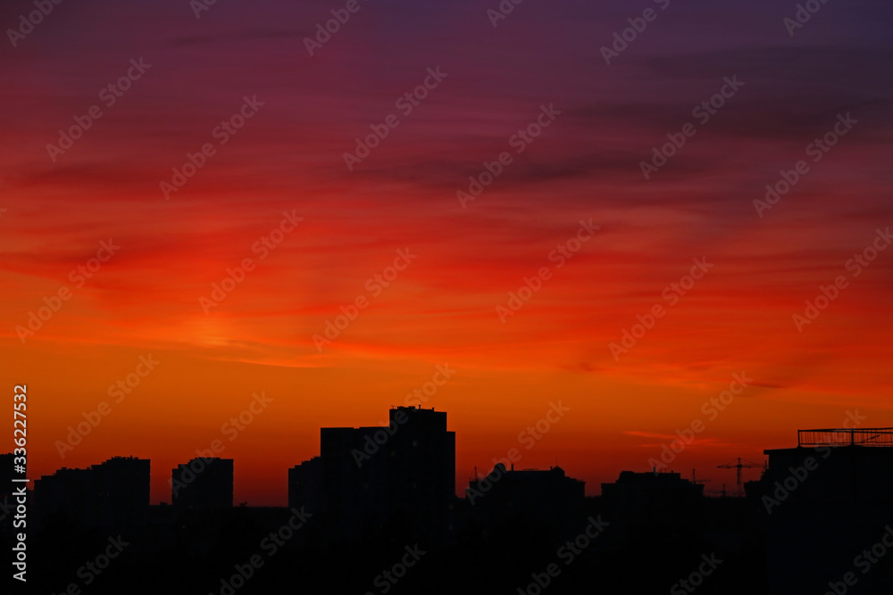 Bright orange sunset over the city in the evening. Bright lights of high-rise buildings of urban buildings. Silhouette of construction city crane of building under construction, selective focus.