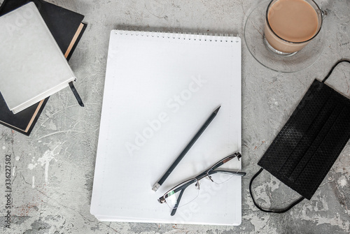 Black medical mask and notebook. Next to a cup of coffee and a pencil. Work from home. Stay at home in quarantine. Coronavirus concept photo