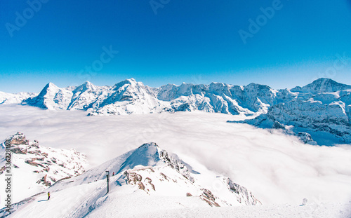 Vista do topo de uma estação de esqui na Suiça com o vale coberto de nuvens e o céu azul © Adriano
