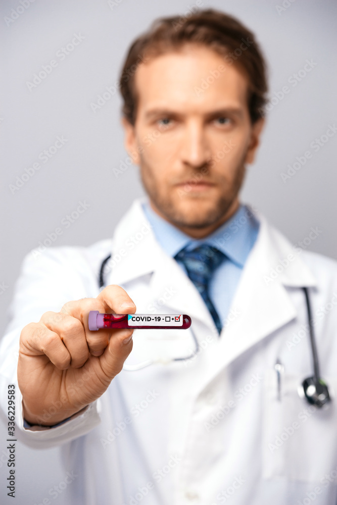 A positive test result for COVID-19. Sad male doctor showing positive blood test result for Coronavirus. Pandemic. Vaccine for COVID-19. Coronavirus outbreak. Blurred vertical image A positive test result for COVID-19. Sad male doctor showing positive blood test result for Coronavirus. Pandemic. Vaccine for COVID-19. Coronavirus outbreak. Blurred vertical image