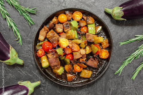 Fried vegetables with meat, vegetables, eggplant, herbs, rosemary on a black background.