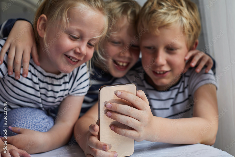 Three children using a smart phone together Three children using a smart phone together