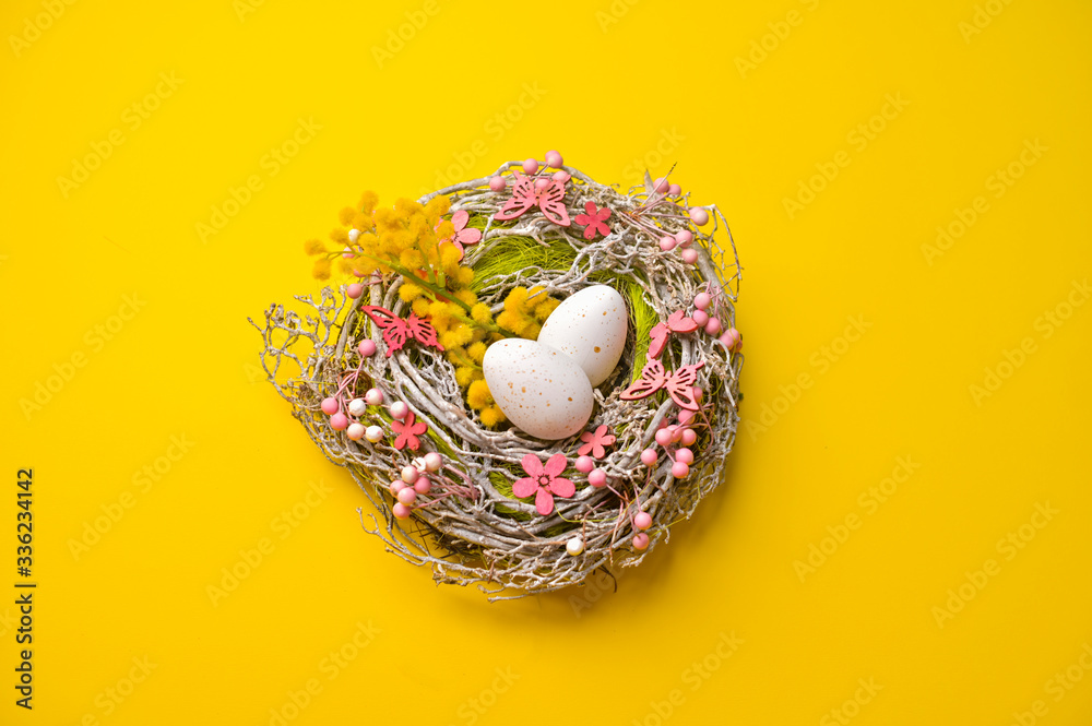 Easter eggs in a basket of flowers and branches on a yellow background. Happy Easter card with copy space for text. Minimal style.